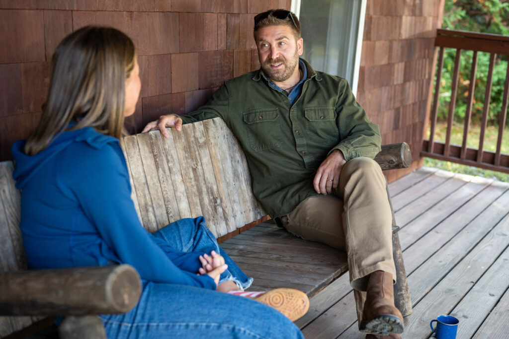 Summit Achievement student an staff conversing on a bench on a porch or a building on campus